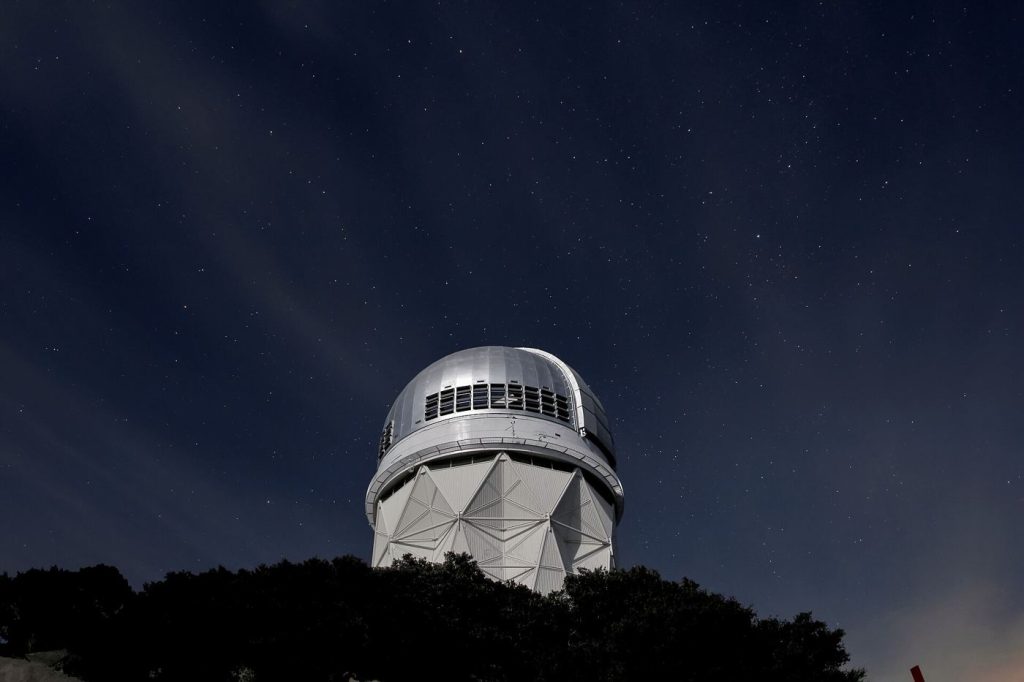 telescope silhouetted under a star-filled night sky